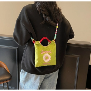 Détail du sac en toile vert avec broderie de donut et bandoulière tressée multicolore