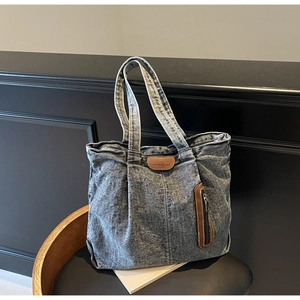 Gros plan détaillé du sac cabas en denim délavé gris foncé avec logo en cuir et poche zippée