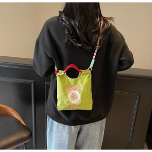 Détail du sac bandoulière en toile verte avec broderie donut et sangle tissée
