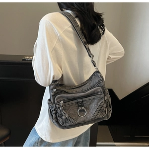 Détail du sac bandoulière en denim délavé avec poches zippées et anneaux en métal