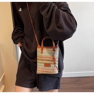 Detail of woven straw crossbody bag with colorful wavy patterns and leather strap