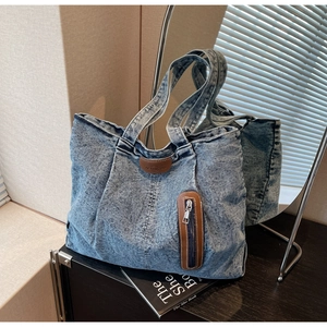 Détail du sac fourre-tout en denim délavé avec écusson en cuir brun et poche zippée