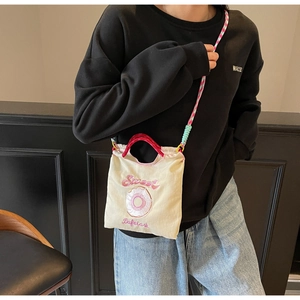 Détail du sac bandoulière en toile crème avec broderie de beignet et sangle rose