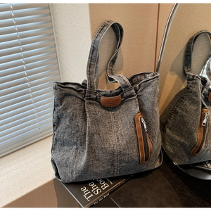 Détail du sac fourre-tout en denim délavé gris avec logo en cuir marron et poche zippée