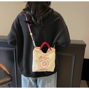Détail du sac en toile avec broderie sweet, sangle colorée et poignée rouge sur modèle