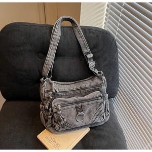 Détail d'un sac bandoulière en denim gris délavé avec poches zippées sur une chaise en velours