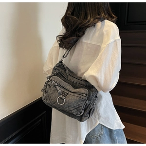 Détail du sac bandoulière en denim gris avec plusieurs poches et anneau sur le mannequin