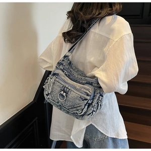 Sac bandoulière en denim bleu avec plusieurs poches zippées et détail d'anneau en métal