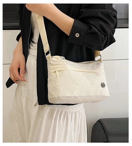 Detailed macro view of cream nylon fabric texture and round metal logo on crossbody bag