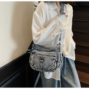 Détail du sac bandoulière en jean délavé avec poches zippées et anneau métallique décor