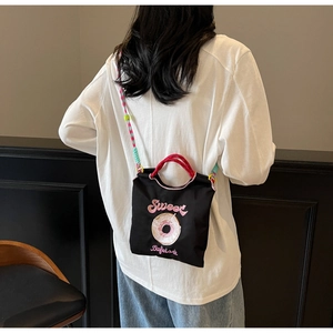 Détail du sac bandoulière noir avec broderie donut rose et sangle tissée colorée