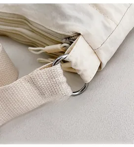 Close-up of durable metal D-ring buckle and zipper detail on beige nylon shoulder bag