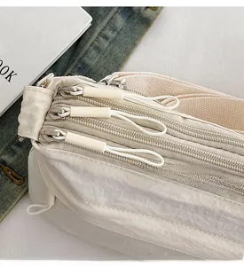 Close-up of triple zipper compartments and nylon fabric on cream crossbody bag