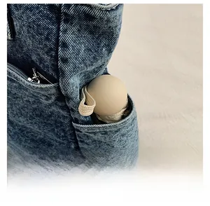 Detail of a blue denim tote side pocket featuring a small cream capsule umbrella