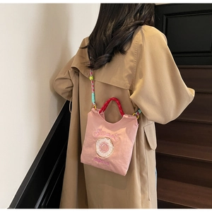 Détail du sac bandoulière rose en toile avec broderie donut et bandoulière tressée colorée