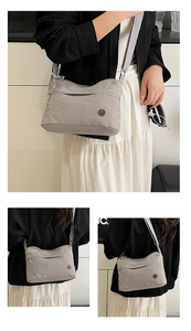 Detail view of water-resistant light grey nylon crossbody bag with zipper pocket and metal logo