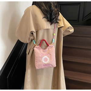 Détail du sac bandoulière en toile rose avec broderie doughnut et poignées rondes rouges
