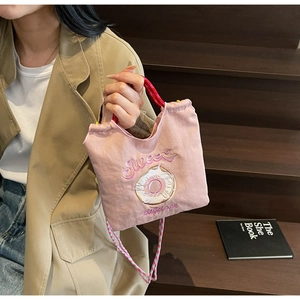 Détail du sac en toile rose avec broderie donut et bandoulière tissée sur un modèle