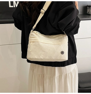 Detail of cream nylon crossbody bag showing the adjustable strap and metallic logo