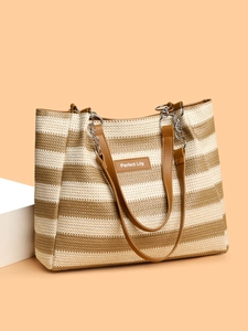 Detail of striped woven straw tote bag featuring leather logo patch and metal chain strap