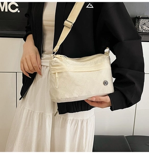 Detail view of cream nylon crossbody bag with multi-zipper layers and adjustable strap
