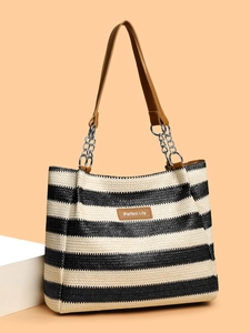 Close-up of black and white striped straw tote bag with brown leather label and chain strap