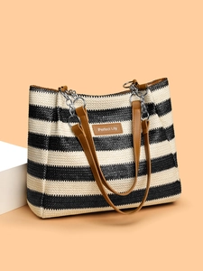 Detail of woven straw tote bag featuring a leather logo patch and metal chain strap