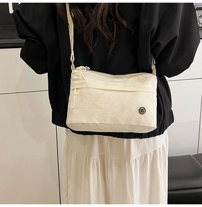 Detail of a beige nylon crossbody bag with a circular logo patch and zipper closure