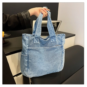 Detail of light blue denim tote bag featuring dual handles and large front utility pocket
