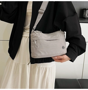 Detail of grey waterproof nylon crossbody bag showing zippers and adjustable shoulder strap
