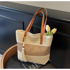 Detail der gestreiften Stroh-Tote-Bag mit Perlen-Quasten-Anhänger auf einem Holzstuhl