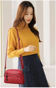Detail of red quilted PU leather crossbody bag featuring dual zippers and adjustable strap