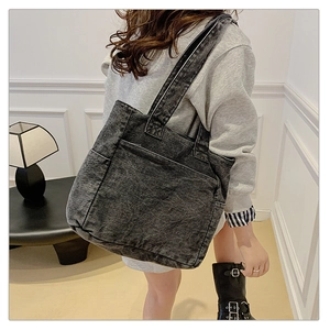 Detail of dark gray washed denim tote bag with large front pocket and long shoulder straps