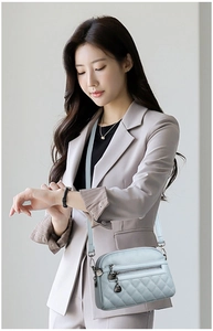 Close-up of light blue quilted crossbody bag with metal logo charm on a beige suit