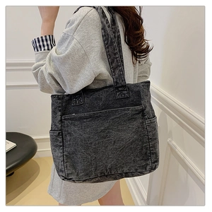 Detail of a dark grey denim tote bag with large pockets and wide shoulder straps