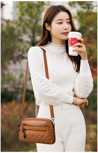 Close-up of brown quilted leather crossbody bag featuring a multi-zippered design