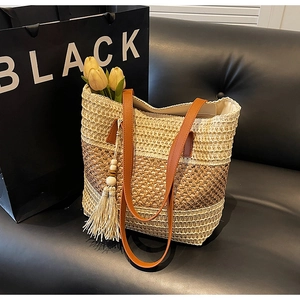 Detail der handgewebten Stroh-Tote-Bag mit braunen Ledergriffen und Holzperlen-Quasten