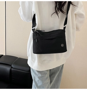 Side view of black nylon crossbody bag on model showing adjustable strap and silver logo