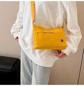 Detail of yellow nylon crossbody bag featuring adjustable strap and circular logo emblem