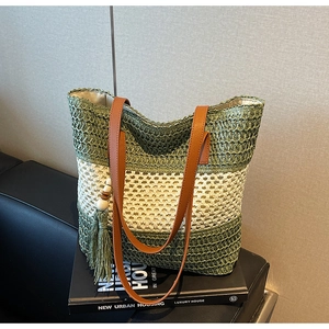 Detail einer grün-beigen Stroh-Tasche mit Ledergriffen und Quastenanhänger aus Holzperlen