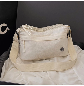 Detail of water-resistant cream nylon crossbody bag with multiple zip pockets and logo