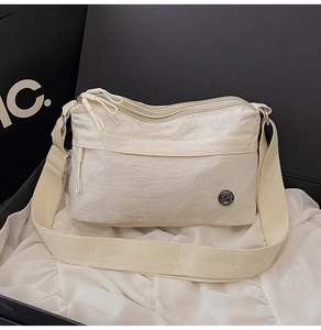 Detail view of cream nylon crossbody bag with multi-zipper layers and adjustable strap