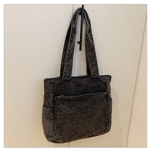 Detail of washed black denim tote bag featuring large front pocket and durable handles