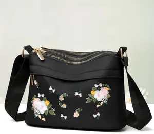 Detailed embroidery on a black nylon crossbody bag with three golden metal zippers