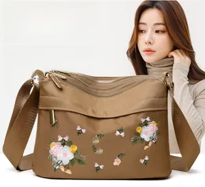Detail of floral embroidery and multi-layer zippers on khaki nylon shoulder bag