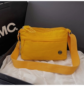 Detail of yellow nylon crossbody bag with wide strap and round metal logo on display