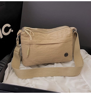 Detail of light khaki nylon crossbody bag with three zipper pockets on silk fabric