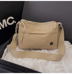 Detailed close-up of beige nylon crossbody bag with multi-zipper pockets on silk