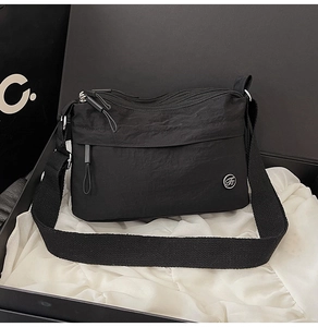 Detail view of water-resistant black multi-pocket crossbody bag with logo on a gift box