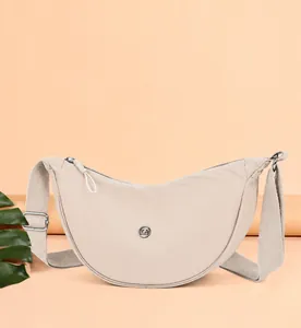 Dettaglio frontale della borsa a mezzaluna in nylon beige con tracolla larga regolabile